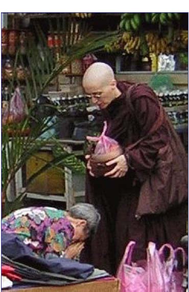 [A woman bows at Ayya Medhanandi's feet after offering a bag of food]